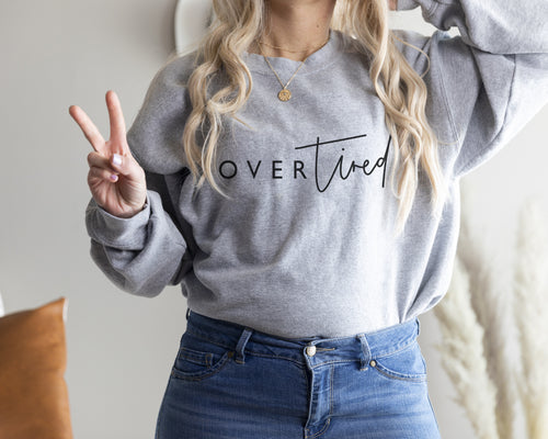 grey sweatshirt worn by blonde model featuring overtired slogan in black