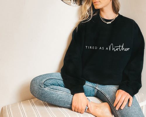 black sweater featuring the slogan tired as a mother in white 
