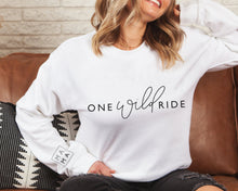 Load image into Gallery viewer, white jumper featuring one wild ride slogan in black with MAMA logo on sleeve worn by blonde model in ripped black jeans sat on a tan leather sofa
