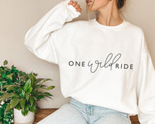 Load image into Gallery viewer, White jumper with one wild ride slogan in black - worn but model in light wash blue jeans sat on desk next to plants

